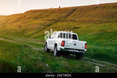 Volkswagen Amarok blanc près de la colline verte. Vue arrière d'un pick-up VW à cabine double sur un chemin de terre parmi les collines. Banque D'Images