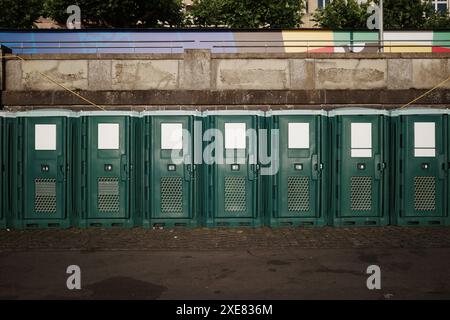 Une vue directe d'une rangée de toilettes portatives vertes alignées contre un mur de béton. Banque D'Images