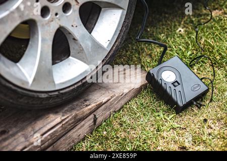 Compresseur d'air portatif gonflant un pneu de voiture reposant sur une planche de bois dans une zone herbeuse Banque D'Images