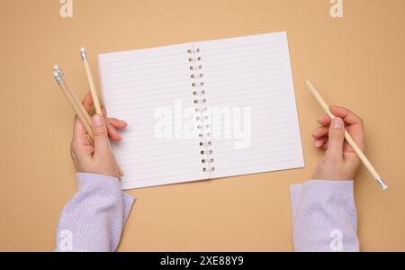 Ouvrez le carnet avec des feuilles blanches vides et la main d'une femme tenant un stylo en bois sur un fond jaune Banque D'Images