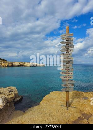 Panneau de direction des capitales européennes sur une planche de bois dans la côte contre ciel nuageux Banque D'Images