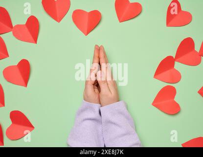 Les mains de la femme pliées dans une pose de prière sur un fond vert avec des cœurs rouges Banque D'Images