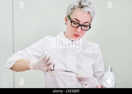 Médecin portant des gants à l'aide d'une pince chirurgicale pour ouvrir le pansement Banque D'Images