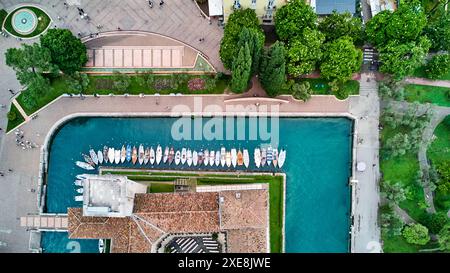 Riva del Garda, Lac Garada, Italie - 25 juin 2024 : vue plongeante sur les toits de Riva del Garada, bateaux et bateaux accostent dans une rangée sur la promenade, de la station. *** Über den Dächern von Riva del Garada aus der Vogelperspektive, Boote und Schiffe legen an der Promenade in einer Reihe an, des Urlaubsortes. Banque D'Images