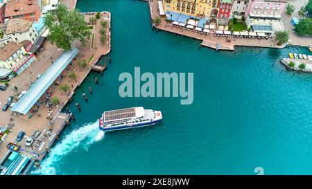 Riva del Garda, Lac de Garde, Italie - 25 juin 2024 : Navigazione Lago di Garda ferry ou bateau dans le port historique de Riva del Garda sur le Lac de Garde, entre bâtiments traditionnels et restaurants. *** Navigazione Lago di Garda Fähre, bzw. Schiff im Hafen vom historischen Riva del Garda am Gardasee, zwischen traditionellen Gebäuden und restaurants. Banque D'Images