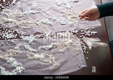 Gros plan des mains féminines de couturière tailleur robe de mariée à coudre à l'aide de perles et de dentelle dans le studio Banque D'Images