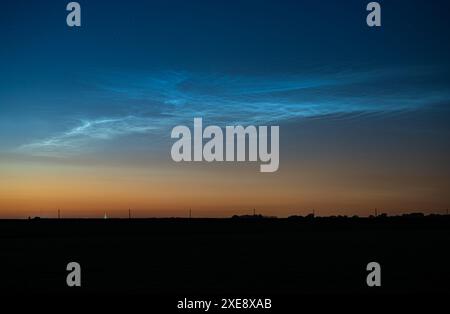 Des nuages noctilucents bleu argenté (NLC) brillants se détachent contre le ciel crépusculaire du soir par une nuit de minuit d'été Banque D'Images