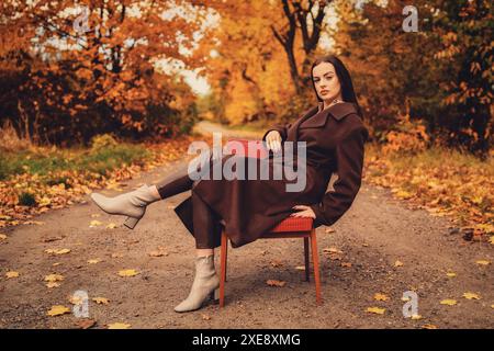 Portrait d'une jeune femme avec un vieux fauteuil dans un manteau brun en automne Banque D'Images