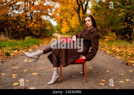 Portrait d'une jeune femme avec un vieux fauteuil dans un manteau brun en automne Banque D'Images