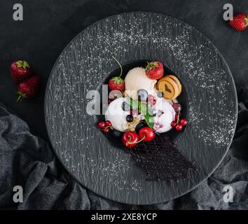 Cuillères à crème glacée à la vanille avec des baies fraîches sur une assiette noire Banque D'Images