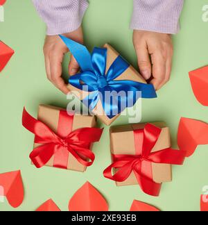 Main de femme tenant une boîte cadeau enveloppée dans un ruban de soie rouge sur un fond vert, vue de dessus Banque D'Images