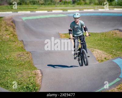 Enfant sur le vélo bmx sur la piste de pompe. Jeune cycliste masculin dans le casque et la protection monte bmx vélo sur la piste de course de vélo asphaltée. Boy BMX rider s'amusant et s'entraînant sur la piste de vitesse de course. Sport extrême Banque D'Images