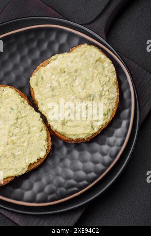 Pain grillé avec pâte d'avocat, œufs, fromage à la crème, sel, épices et herbes Banque D'Images