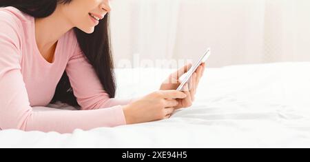 Femme allongée sur le lit regardant le téléphone portable, recadrée Banque D'Images