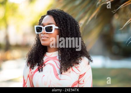 Femme aux cheveux bouclés portant des lunettes de soleil blanches à l'extérieur Banque D'Images
