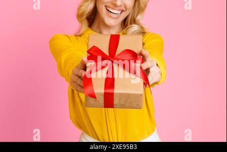 Femme tenant cadeau avec ruban rouge contre rose, rogné Banque D'Images