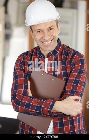 électricien mature avec presse-papiers à côté de la boîte à fusibles Banque D'Images