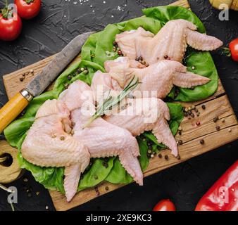 Ailes de poulet crues avec des ingrédients pour la cuisson sur une planche à découper en bois sur fond de pierre sombre Banque D'Images