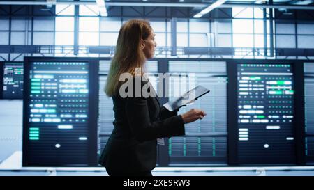 Ingénieur en concentrateur de serveurs vérifiant le plan de reprise sur tablette, surveillant la consommation d'énergie des montages en rack. Femme dans le centre de données s'assurant que les plates-formes fonctionnent de manière optimale, effectuant des contrôles de routine du disque, caméra B. Banque D'Images