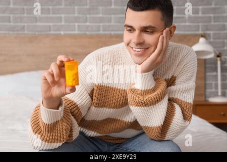 Jeune homme avec bouteille de pilule assis sur le lit dans la chambre Banque D'Images