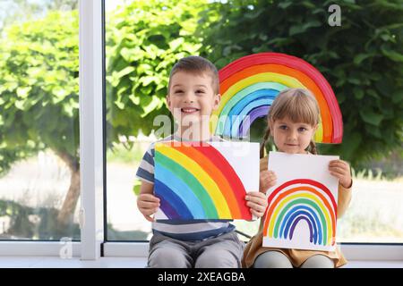 Enfants avec des photos d'arc-en-ciel près de la fenêtre à l'intérieur Banque D'Images