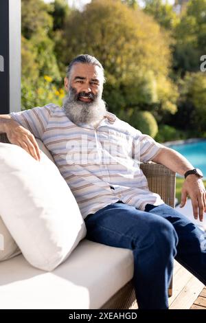 Détente en plein air, homme senior assis sur le canapé-terrasse près de la piscine Banque D'Images