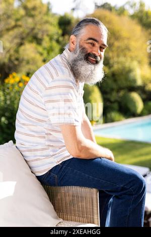 Homme senior souriant assis à l'extérieur, profitant d'une journée ensoleillée au bord de la piscine Banque D'Images