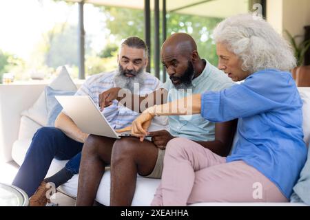 À la maison, groupe d'amis assis sur le canapé, à l'aide d'un ordinateur portable et discutant de quelque chose ensemble Banque D'Images