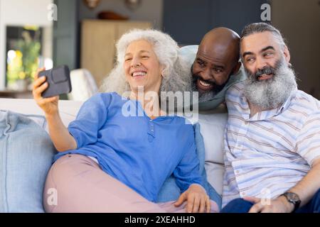 À la maison, prendre selfie, groupe d'amis seniors souriant et assis sur le canapé à l'intérieur Banque D'Images