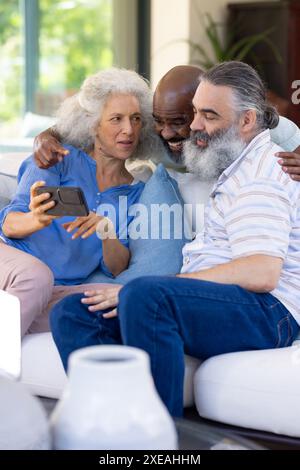 À la maison, groupe d'amis seniors regardant le smartphone ensemble, assis sur le canapé Banque D'Images
