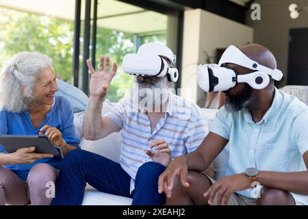 À la maison, groupe diversifié d'amis seniors utilisant des casques VR et une tablette, profitant de la technologie Banque D'Images