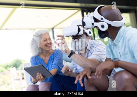 À la maison, des amis seniors utilisant des casques VR et une tablette, profitant de l'expérience de réalité virtuelle Banque D'Images