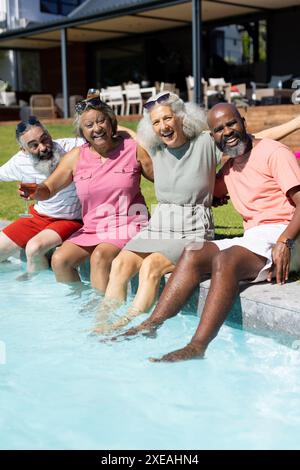 Groupe diversifié d'amis seniors assis près de la piscine, profitant de la journée d'été ensemble Banque D'Images