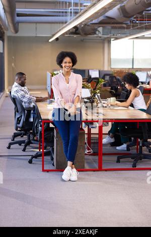 Debout dans un bureau moderne, femme d'affaires souriante avec des collègues travaillant en arrière-plan Banque D'Images