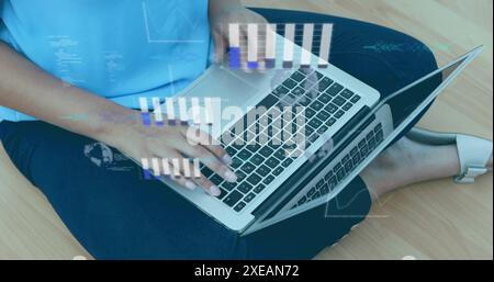 Image de graphiques, globe, langage informatique sur femme biraciale travaillant sur ordinateur portable à la maison Banque D'Images