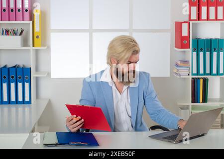 Inspecteur sérieux travaillant avec des dossiers papier presse-papiers et un ordinateur portable. Recherche d'informations commerciales. Rapports, documents. Auditeur masculin Banque D'Images