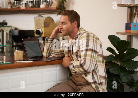 Image d'un homme adulte regardant compliqué à l'écran de l'ordinateur portable, regardant perplexe à son moniteur, faisant une tâche difficile en ligne, assis dedans Banque D'Images