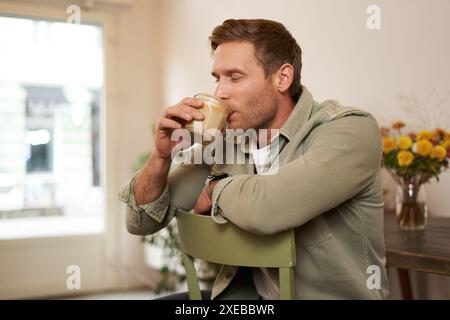 Portrait de bel homme blond dans le café, assis sur la chaise, apprécie le goût d'une délicieuse tasse de café fraîchement infusée Banque D'Images