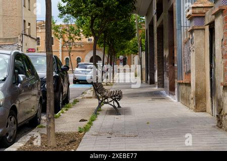 Figueres, Espagne - 14 mai 2023 : une vue sur un trottoir tranquille à Figueres, Espagne avec un banc en bois et des voitures garées. Banque D'Images