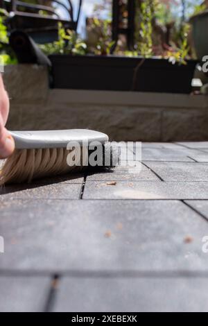 Homme brossant le patio de carreaux de terrasse composite nouvellement posés avec une brosse à main. Concept d'améliorations de la maison de jardin. Banque D'Images