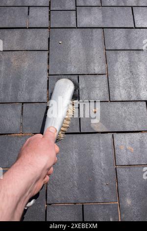 Homme brossant le patio de carreaux de terrasse composite nouvellement posés avec une brosse à main. Concept d'améliorations de la maison de jardin. Banque D'Images