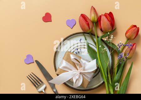 Belle table avec boîte cadeau, coeurs décoratifs et fleurs de tulipes sur fond pêche pastel. Banque D'Images