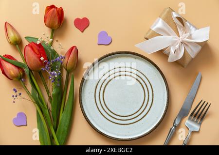 Belle table avec boîte cadeau, coeurs décoratifs et fleurs de tulipes sur fond pêche pastel. Banque D'Images