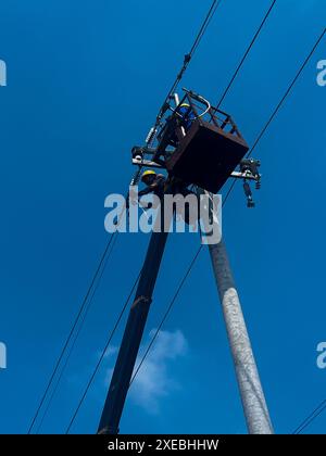 Lineman ou électriciens grimpent sur des poteaux électriques pour installer et réparer des lignes électriques avec un ciel bleu. Ouvriers réparant des lignes électriques Banque D'Images