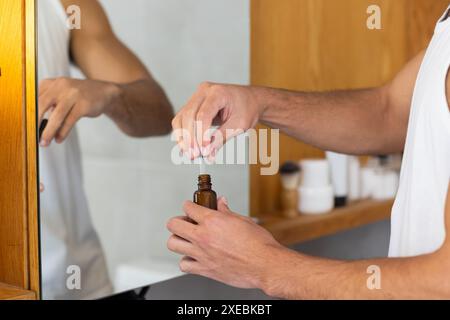 À la maison, appliquer de l'huile de barbe, homme toilettant dans la salle de bain devant le miroir Banque D'Images