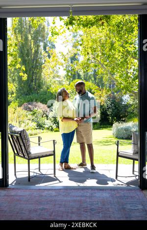 Couple debout sur le patio, se tenant la main et souriant l'un à l'autre Banque D'Images
