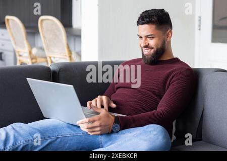 Homme souriant à l'aide d'un ordinateur portable tout en se relaxant sur le canapé à la maison Banque D'Images