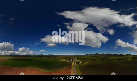 Paysage panoramique avec ciel bleu, nuages moelleux sur des champs verts et une longue route droite Banque D'Images