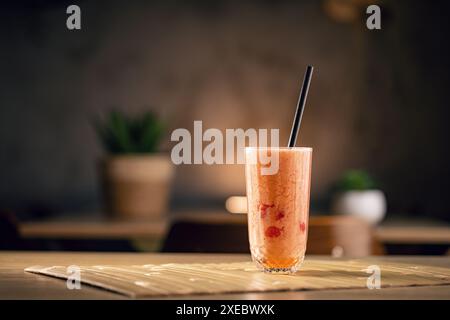 Délicieux smoothie avec des baies rouges et de la paille attend sur une table dans un café Banque D'Images