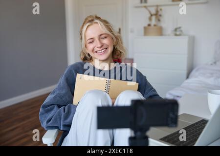 Portrait de femme souriante blonde, enregistre des vidéos sur appareil photo numérique comment elle écrit dans un cahier, parle à des adeptes, fait le style de vie Banque D'Images